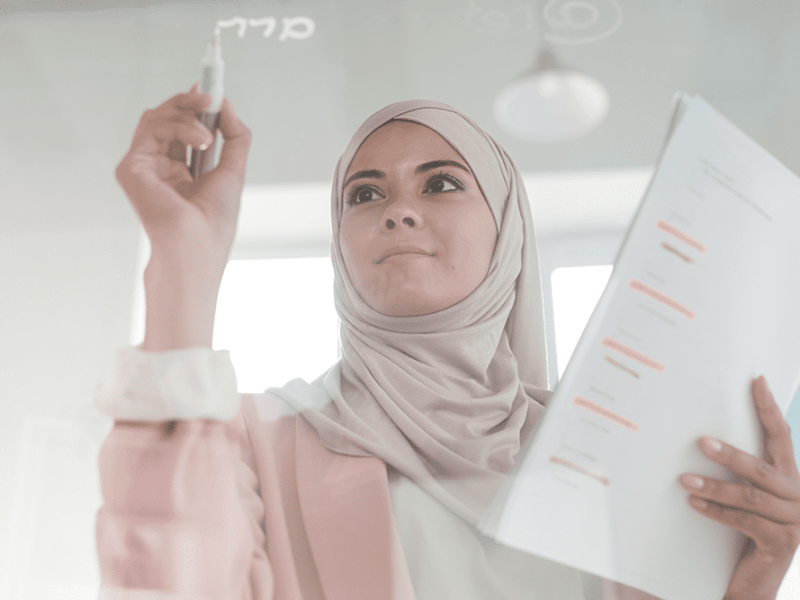 young-serious-female-broker-hijab-holding-financial-papers-highlighter-while-making-presentation-by-transparent-board